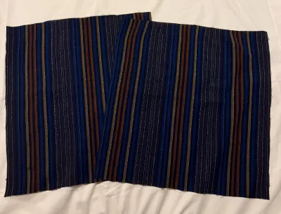 A white fabric background, on top are two panels of a multicoloured woven fabric in a traditional Southeast Asian style.